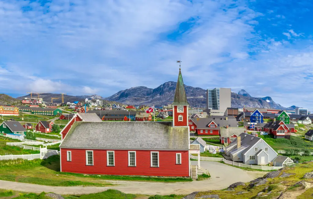 Panoramic view of Nuuk, the capital of Greenland, showcasing its distinctive colorful houses and church against a backdrop of majestic mountains and icebergs.