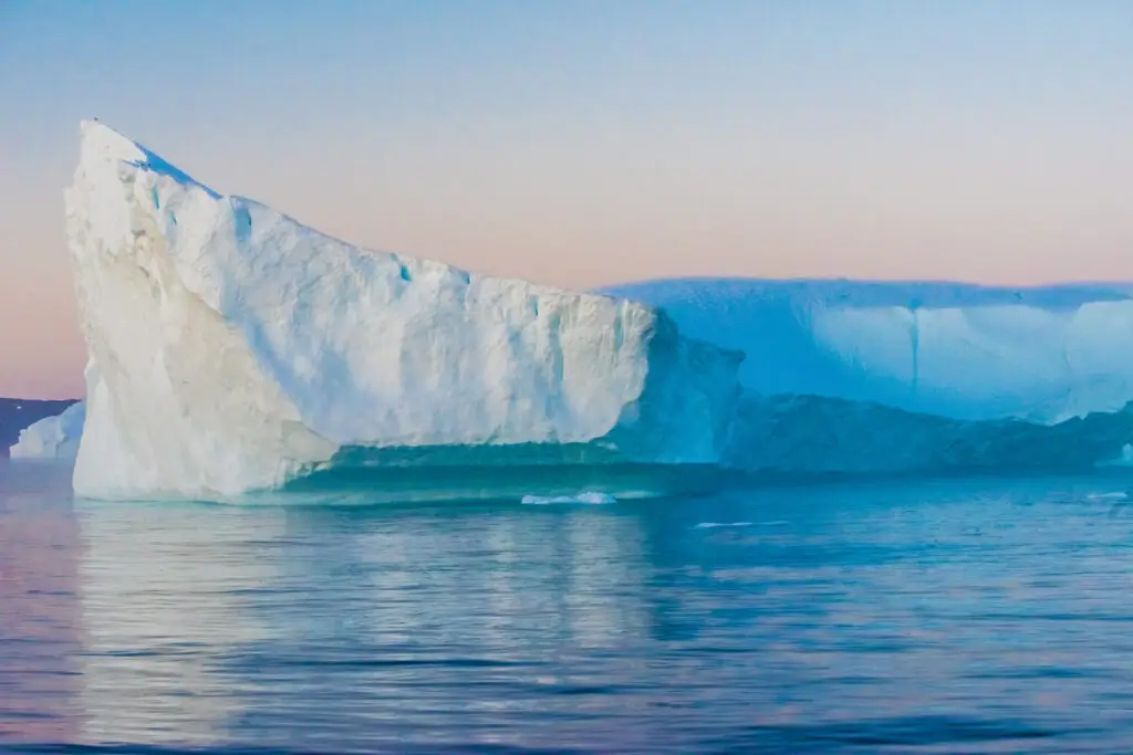 Majestic view of a large iceberg glowing under the midnight sun in Ilulissat, Greenland, reflecting on the serene Arctic waters
