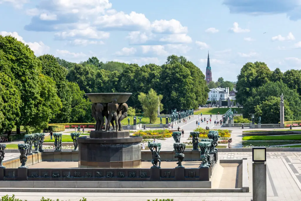 View of the iconic sculptures at Vigeland Park in Oslo, Norway, showcasing an array of bronze statues on a sunny day frequented by visitors.