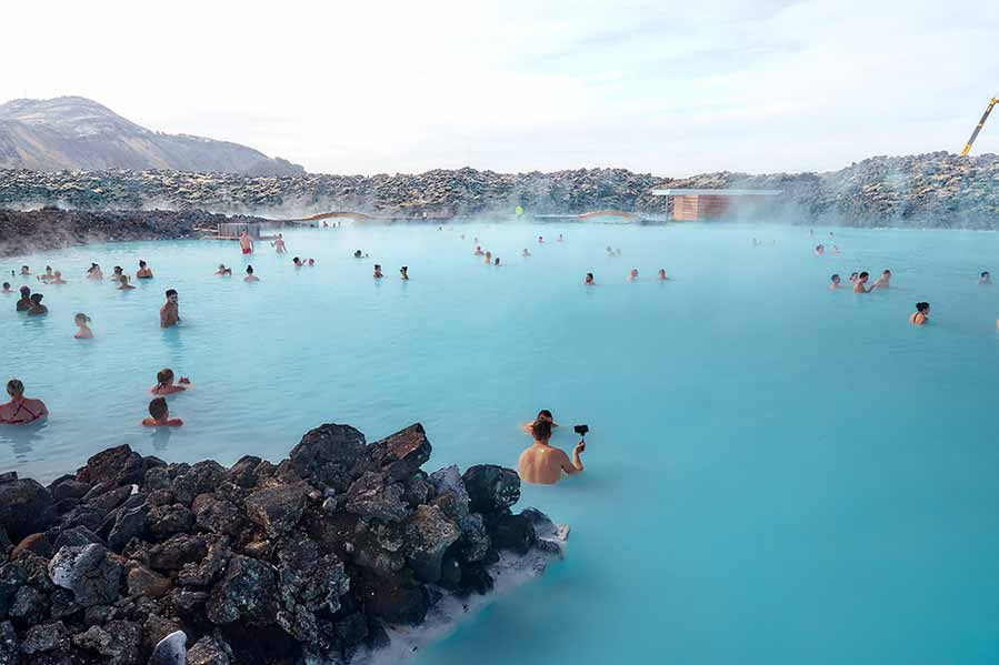 Tourists enjoying a relaxing soak in the geothermal waters of Blue Lagoon, Iceland, surrounded by rugged lava rocks.