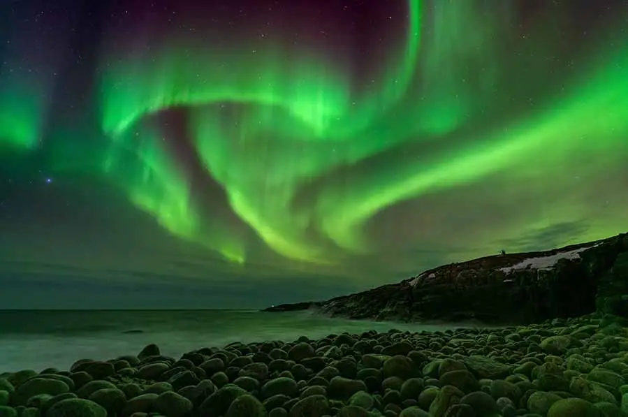 Vivid Northern Lights display over a rocky Icelandic beach under a starry sky