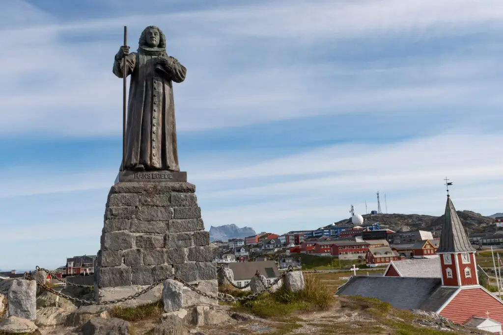 Statue of Hans Egede overlooking colorful houses and a church in Nuuk, Greenland, under a clear blue sky.