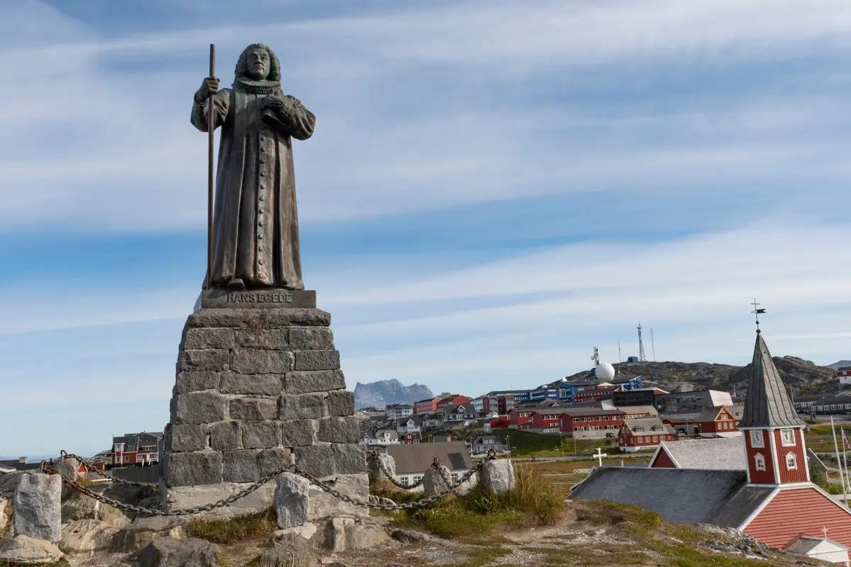Statue of Hans Egede overlooking colorful houses and a church in Nuuk, Greenland, under a clear blue sky.