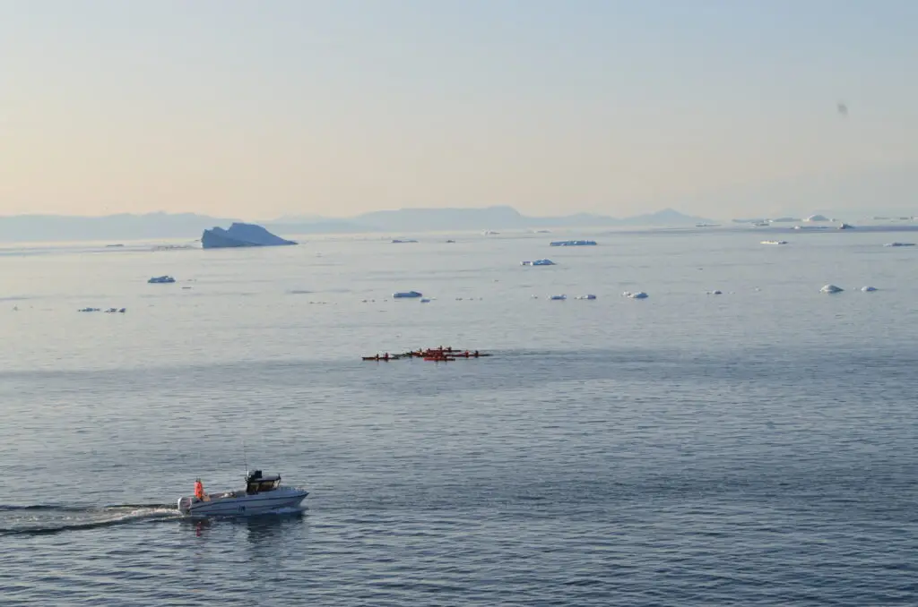 Boat and kayak navigating through icebergs in Ilulissat Icefjord, a popular tourist destination in Greenland