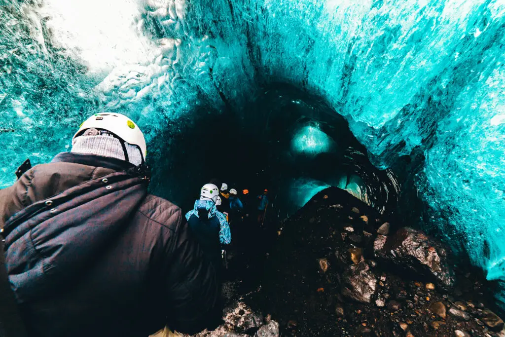 Explorer descending into a stunning blue ice cave in Iceland, showcasing a popular tourist adventure ideal for travelers interested in unique Arctic experiences.