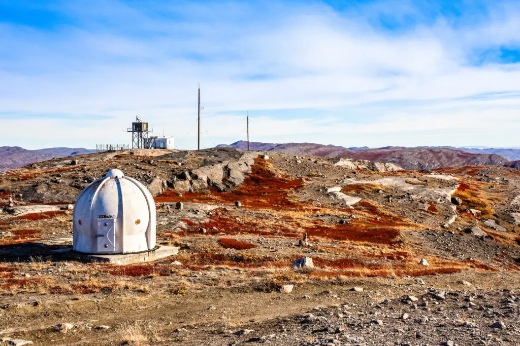 Autumn landscape in Kangerlussuaq, Greenland featuring a metal bunker and meteorologic station on orange tundra with distant mountains