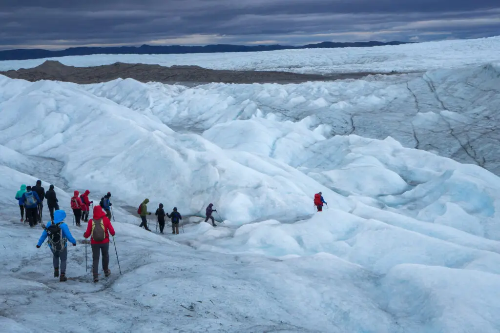 Group of hikers trekking across the vast icecap near Kangerlussuaq in Greenland, showcasing the dramatic icy landscape under a cloudy sky.