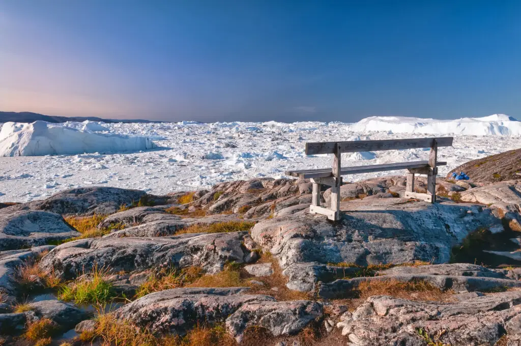 Wooden bench overlooking a breathtaking Icefjord on the hiking trail to Sermermiut, near Ilulissat, Greenland, showcasing serene natural beauty and historical significance.