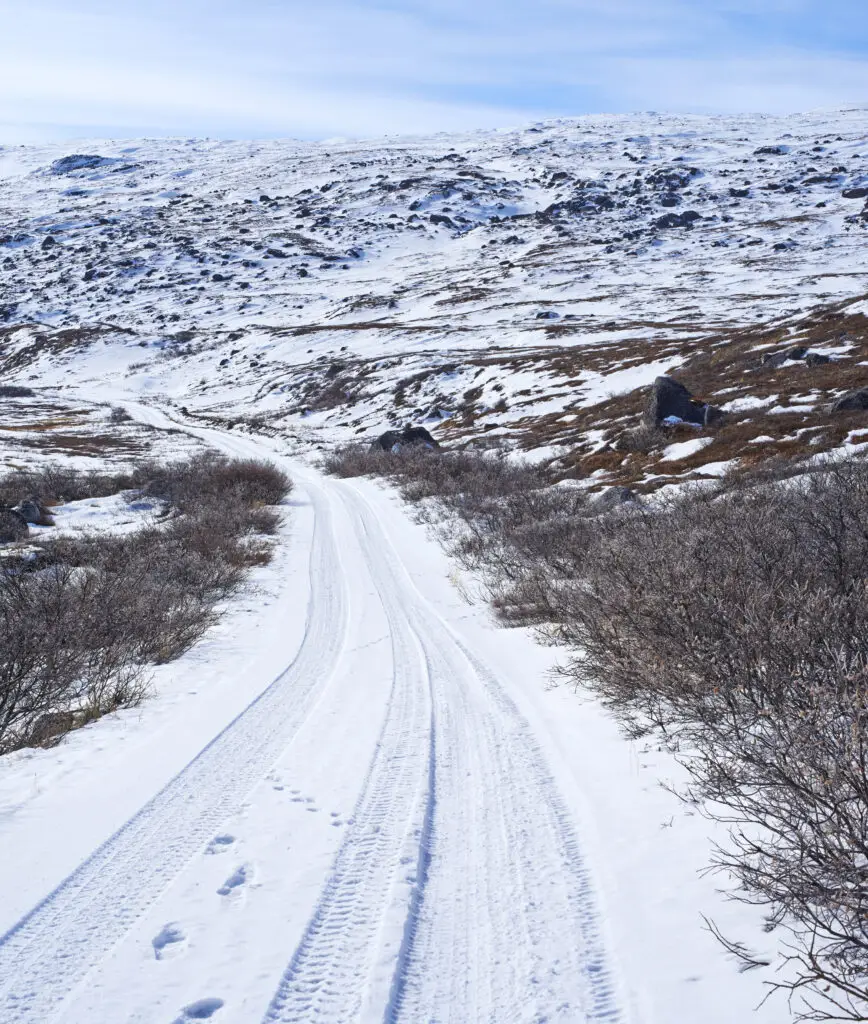 Snowy road winding through the rugged landscape of Kangerlussuaq, Greenland, showing winter in the Arctic with clear blue skies and inaccessible terrain.